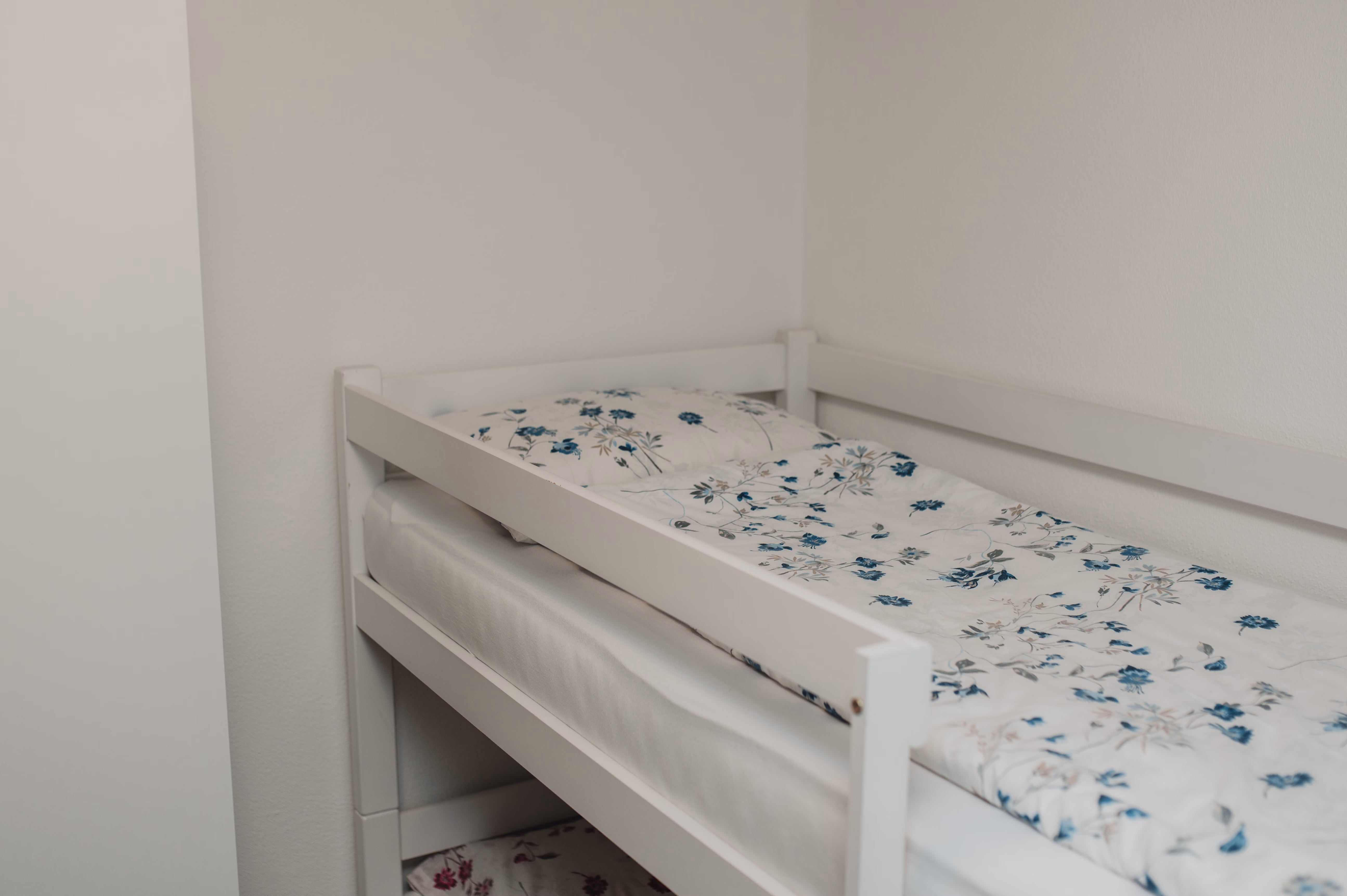Bijeli krevet na sprat s plavom cvjetnom posteljinom u dječijoj sobi