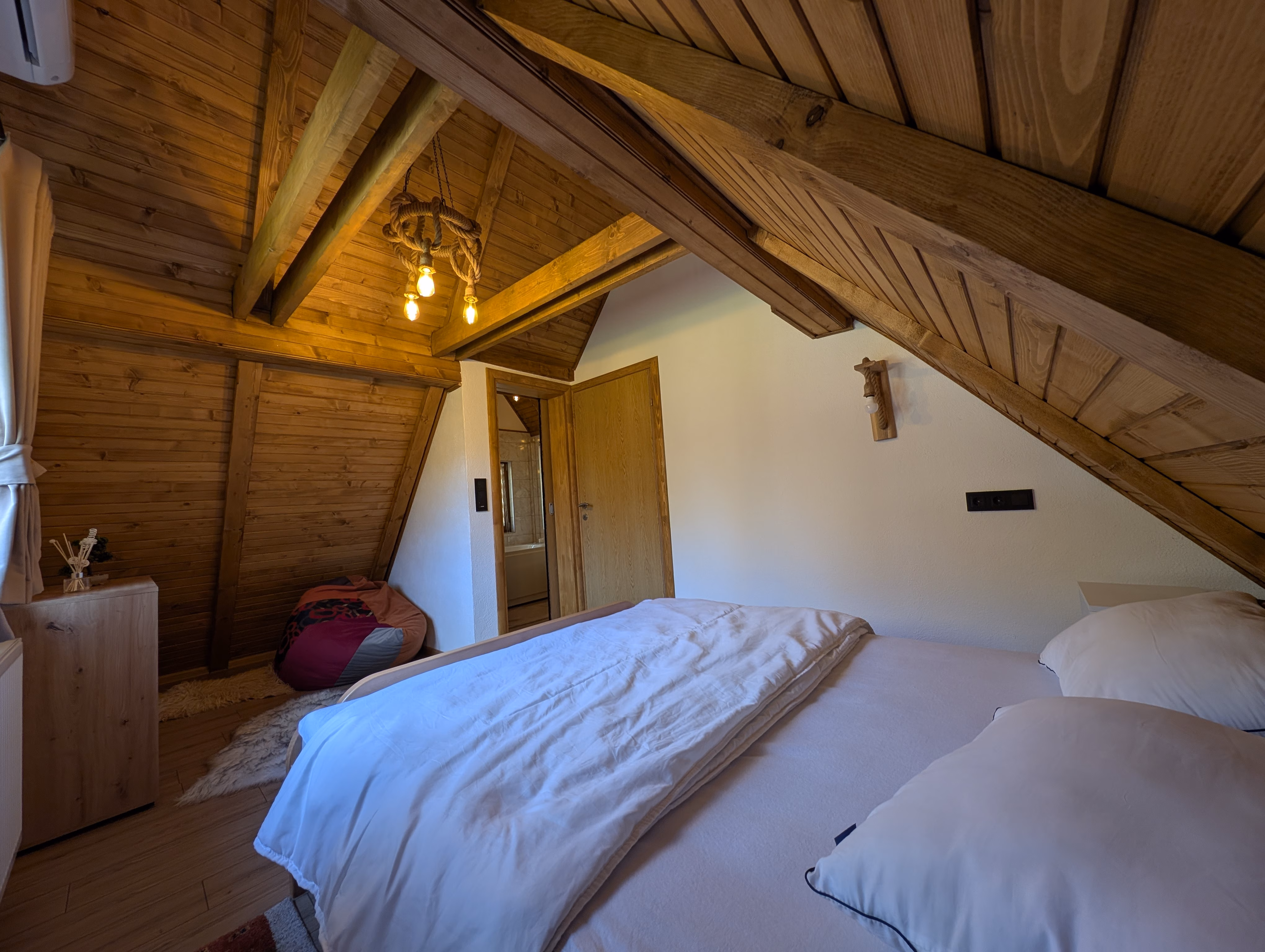 Potkrovna spavaća soba ispod drvenog A-frame stropa s lusterom od užadi