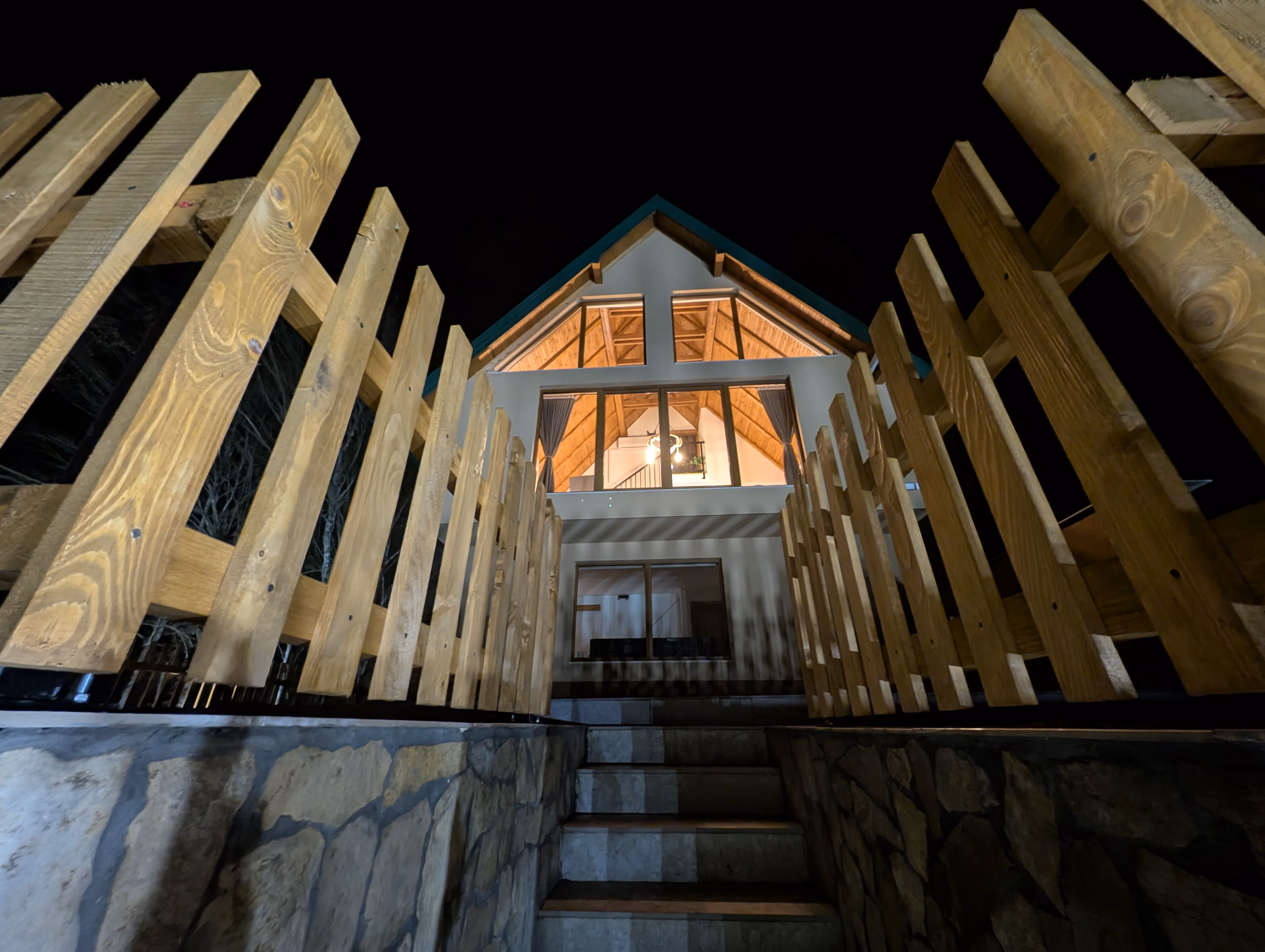 Noćni pogled na ulaz u vilu kroz drvenu ogradu